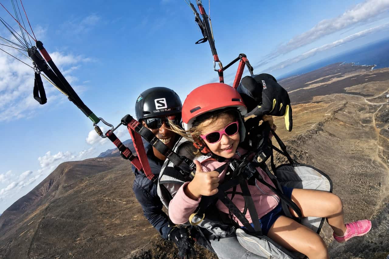 Young girl enjoying a tandem paragliding experience over Lanzarote with an instructor, surrounded by volcanic landscapes and ocean views.