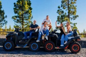 Group of people posing on quads during a private quad trip in Tenerife with pine trees and mountain scenery in the background.