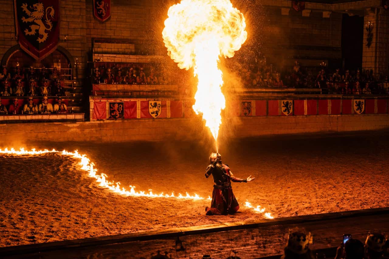 Fire breather performing a spectacular flame display in the arena during the Medieval Adventure Dinner Show in Tenerife, surrounded by a ring of fire.