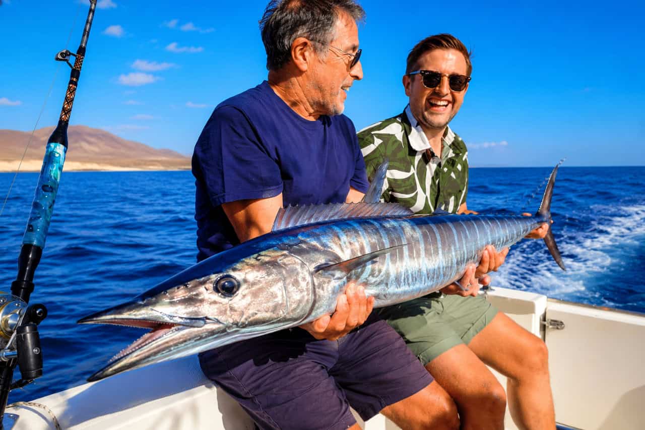 Two anglers holding a large wahoo caught on a deep sea fishing trip from Caleta de Fuste
