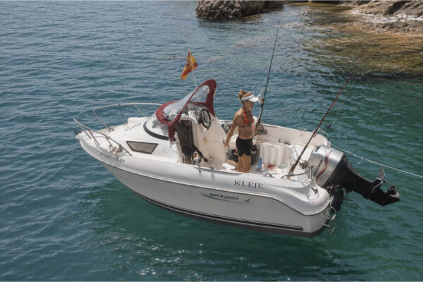 Small private motorboat anchored in clear waters off Gran Tarajal, Fuerteventura, with a guest on board preparing for fishing and snorkelling.
