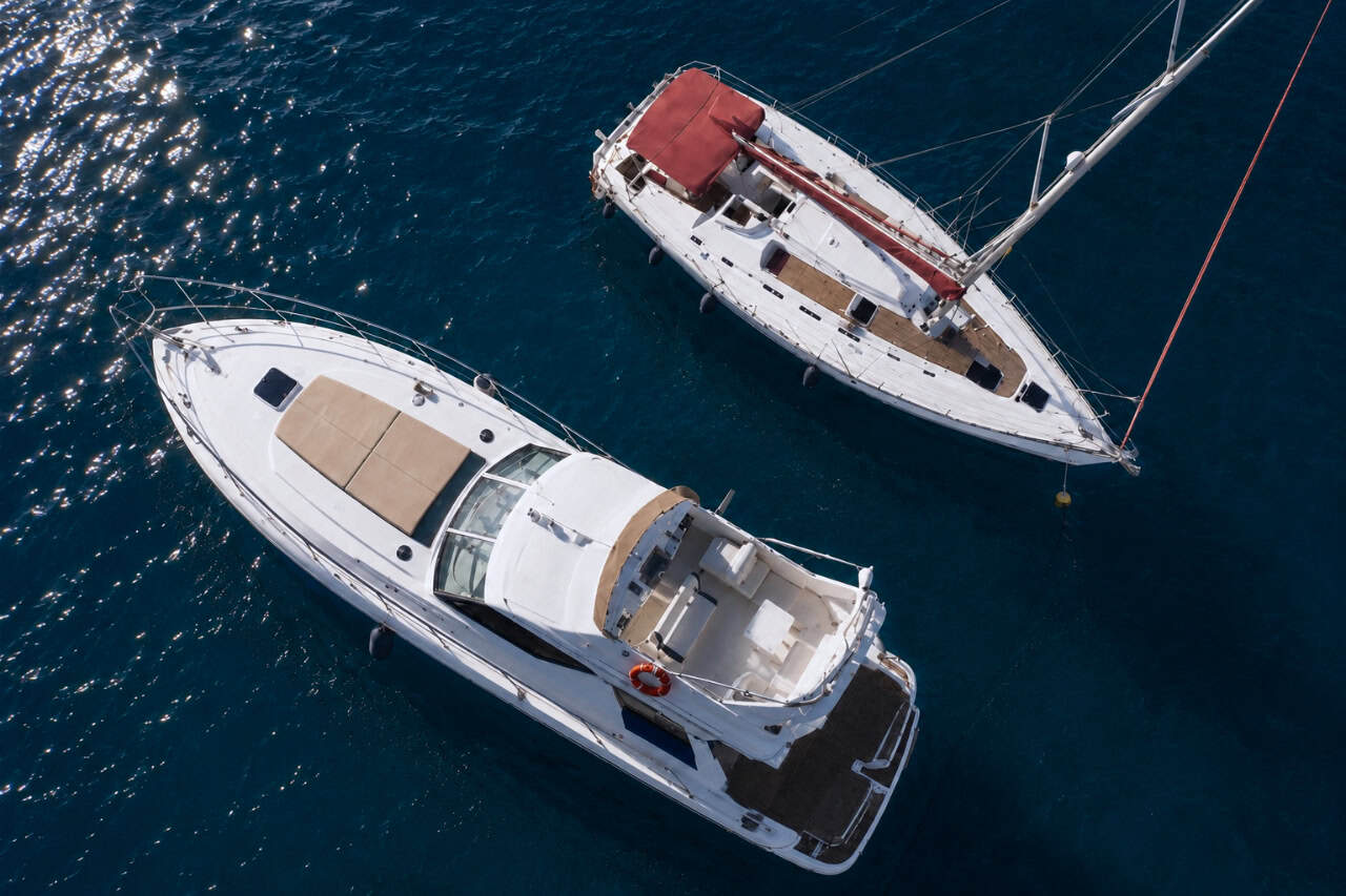 Aerial view of a luxury motor yacht and an elegant sailing yacht anchored side by side in the crystal-clear waters off Tenerife during a peaceful golden hour cruise.
