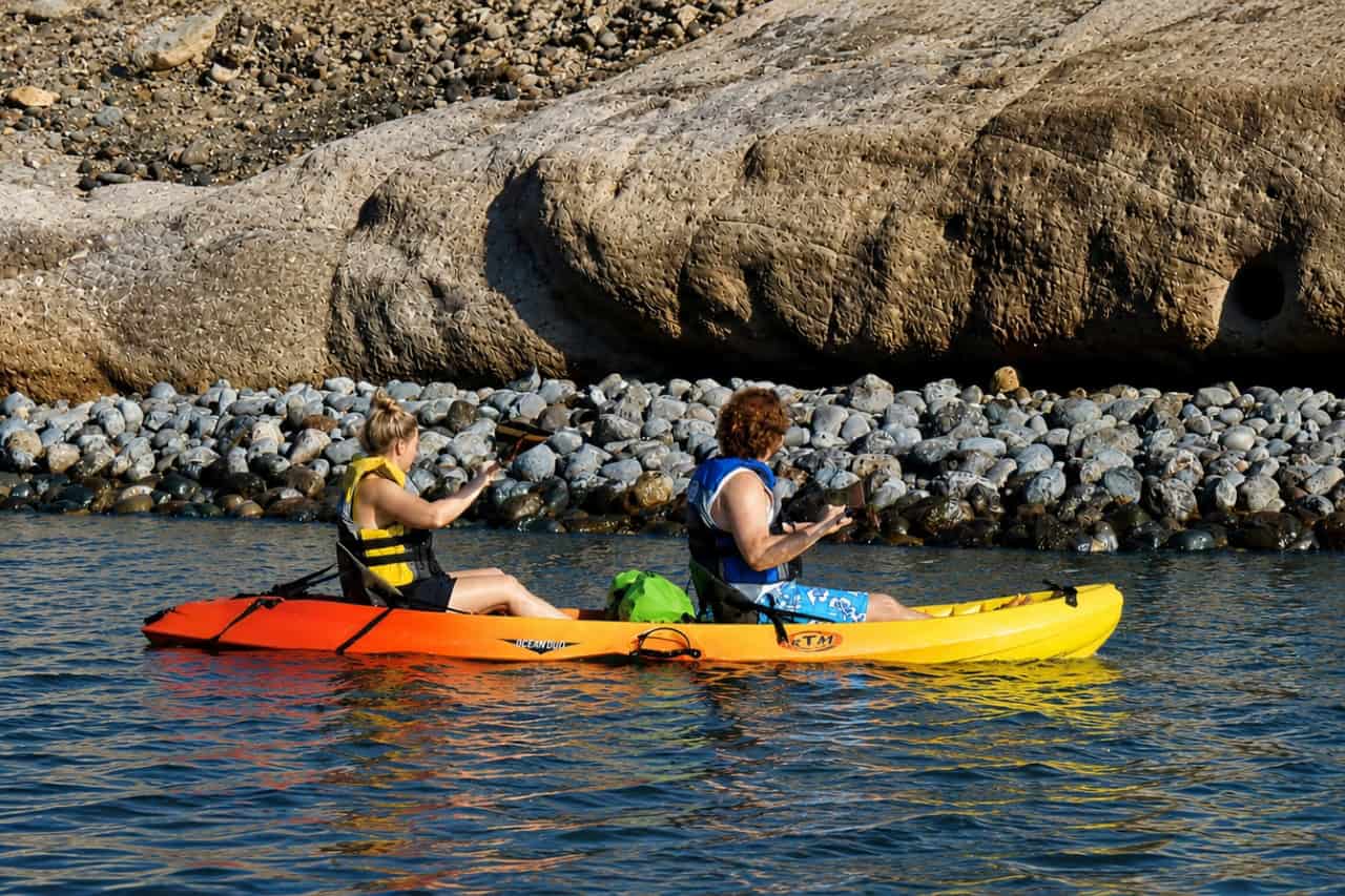 Two people paddling a tandem kayak along the rocky coastline of Gran Canaria during a guided sea kayaking excursion
