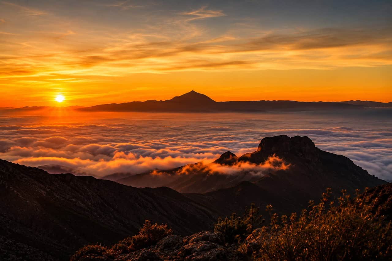 Panoramic view of Gran Canaria's mountains above a sea of clouds during a vibrant golden sunset.
