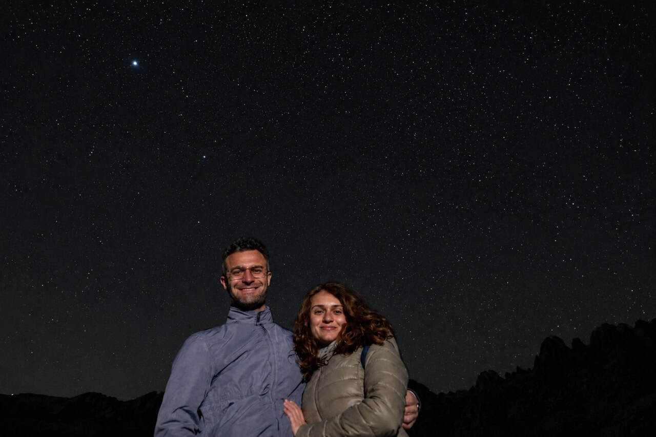Couple standing together beneath a clear, star-filled night sky during a stargazing experience in Gran Canaria, surrounded by a peaceful mountain landscape.