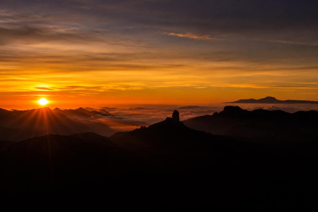 Golden sunset over the volcanic mountains of Gran Canaria with dramatic cloud layers and panoramic views above the clouds.