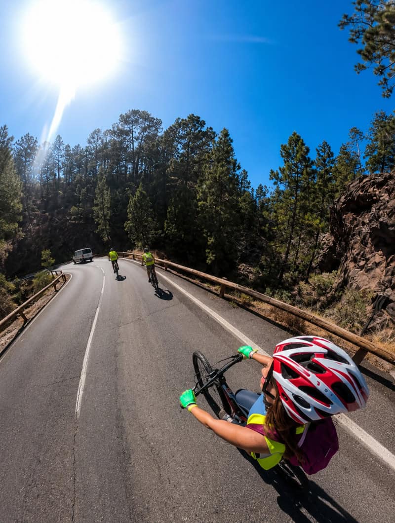 Guided Downhill Bike Tour Through Mount Teide Cyclists following the guide down a winding mountain road, with a support van carrying spare equipment behind the group.