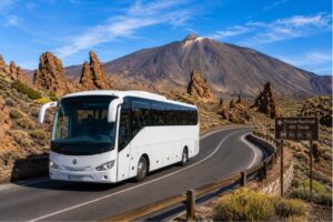 Modern tour coach driving through Teide National Park with Mount Teide and the Roques de García rock formations in the background on a scenic Tenerife road.