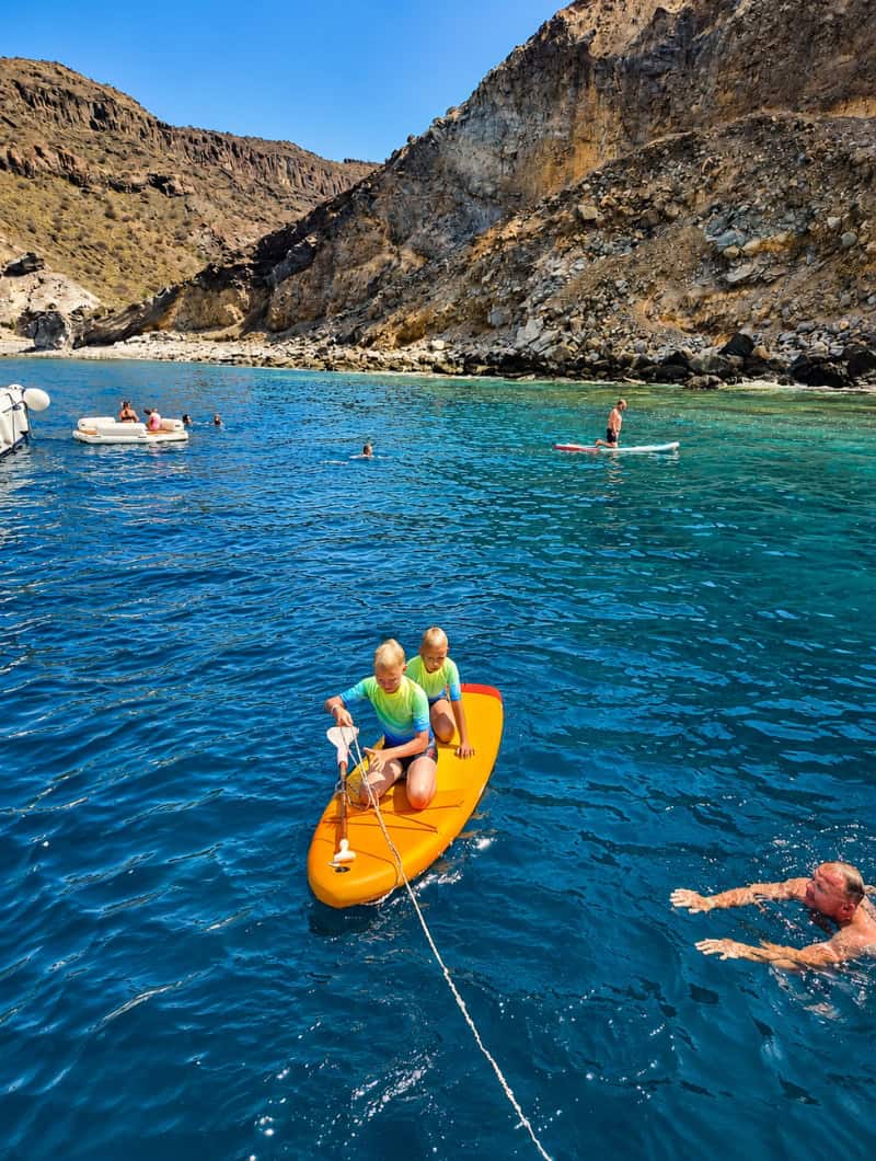 Guests paddle boarding and swimming in a calm bay on a private Karolka charter in Gran Canaria