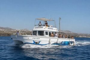 Katfish Express excursion boat cruising along the coast of Lanzarote with passengers on board, offering fishing trips and sightseeing against a backdrop of volcanic landscapes and the Atlantic Ocean.