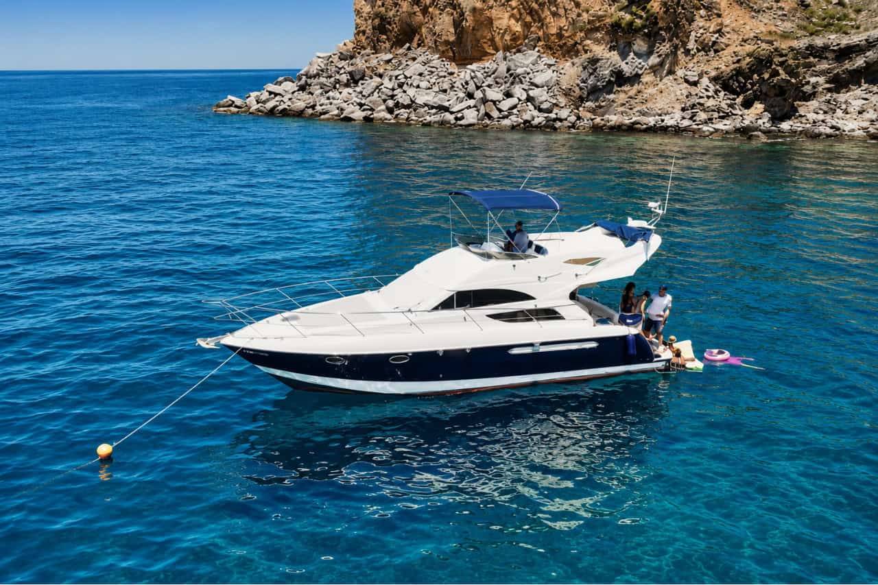 Luxury private motor yacht anchored in a crystal-clear bay on Tenerife's southwest coast, with guests enjoying a swim stop beside the yacht.