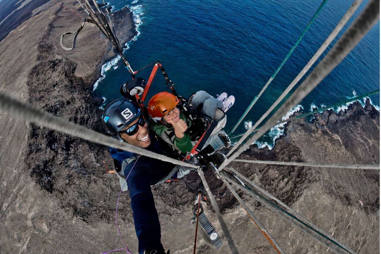 Child giving a thumbs-up during a tandem paragliding flight over Lanzarote’s dramatic volcanic coast with an experienced instructor.