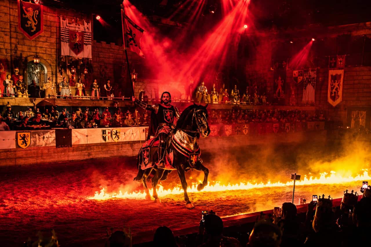 Knight riding a horse through a ring of fire during the Medieval Adventure Dinner Show in Tenerife, with spectators watching the live performance.