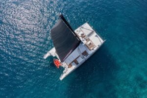 Aerial view of a luxury white catamaran with a black sail cruising over the crystal-clear turquoise waters of Tenerife, offering an exclusive private sailing experience.