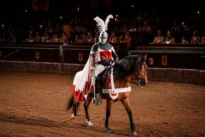 Armoured medieval knight riding a horse during a live jousting performance at Castillo San Miguel in Tenerife, surrounded by spectators in a traditional arena.