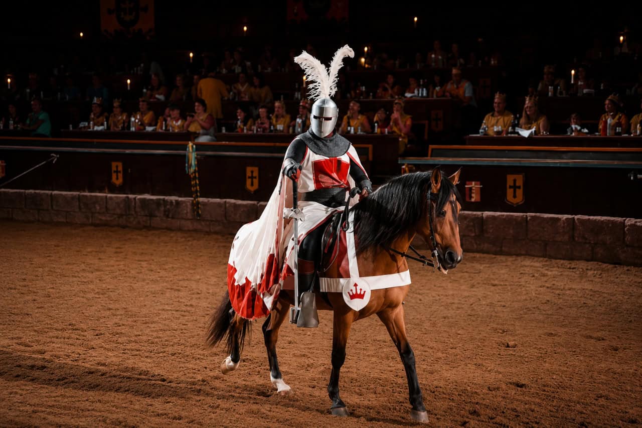 Armoured medieval knight riding a horse during a live jousting performance at Castillo San Miguel in Tenerife, surrounded by spectators in a traditional arena.