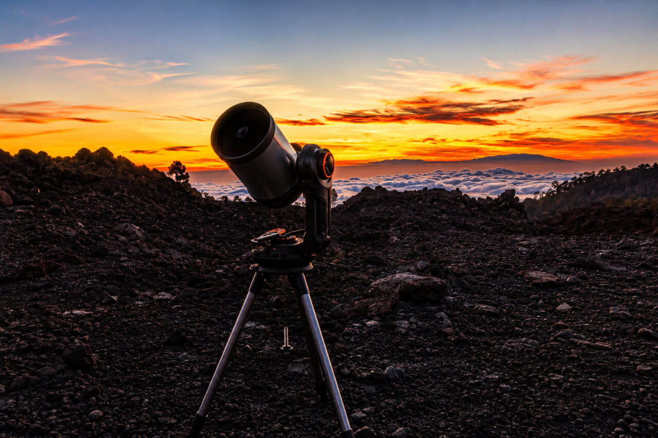 Telescope set up on volcanic terrain above a sea of clouds during a colorful sunset near Mount Teide in Tenerife.