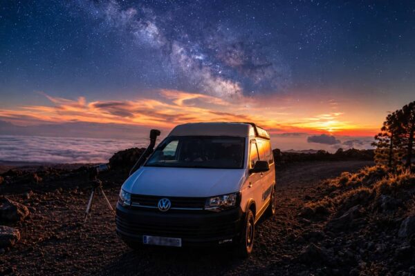 White camper van parked above the clouds at sunset with a telescope set up beside it, ready for a guided stargazing experience.