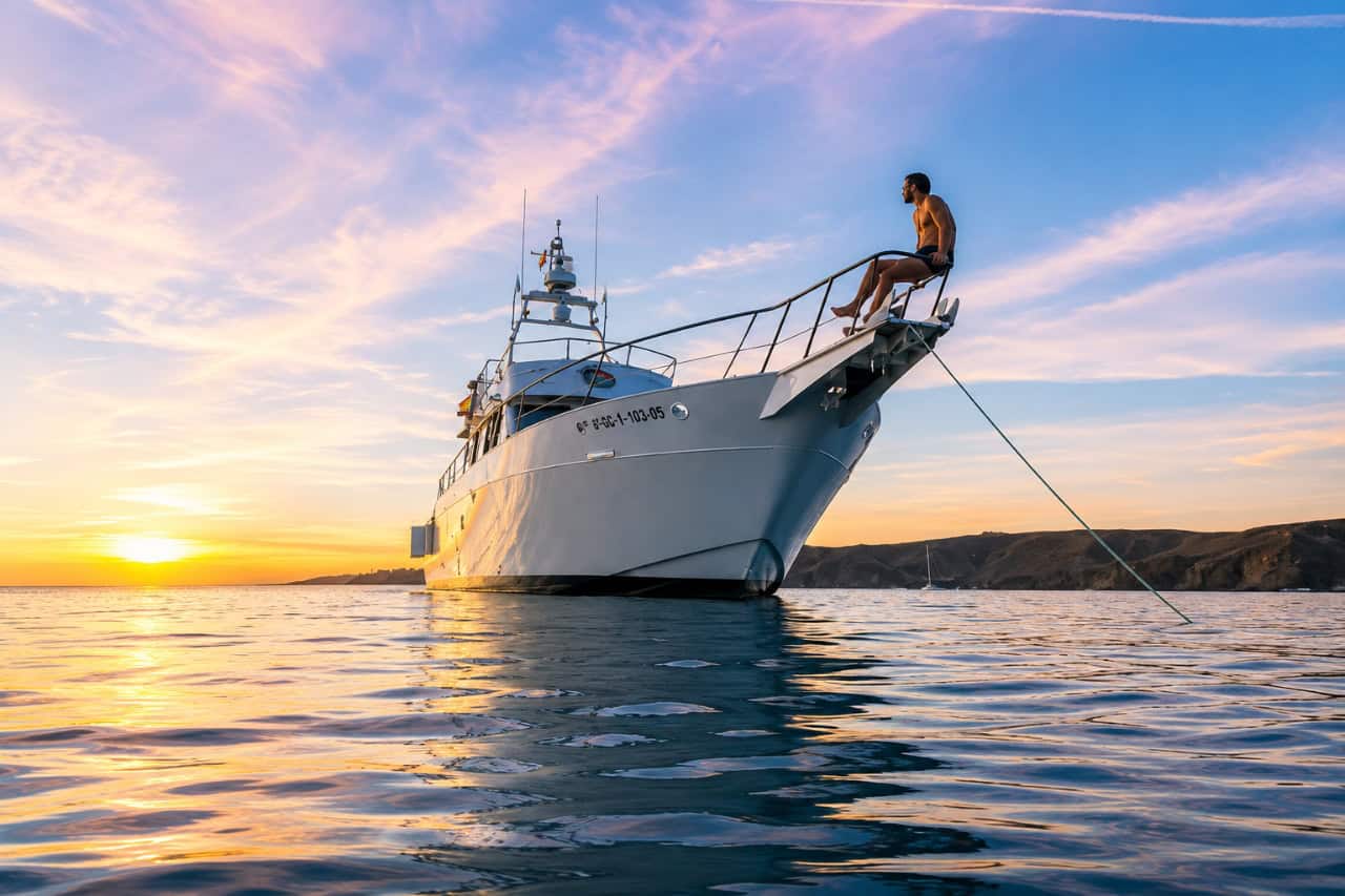 Luxury private yacht anchored off the coast of Tenerife at sunset, with a guest relaxing on the bow and enjoying panoramic ocean views during an exclusive yacht charter.