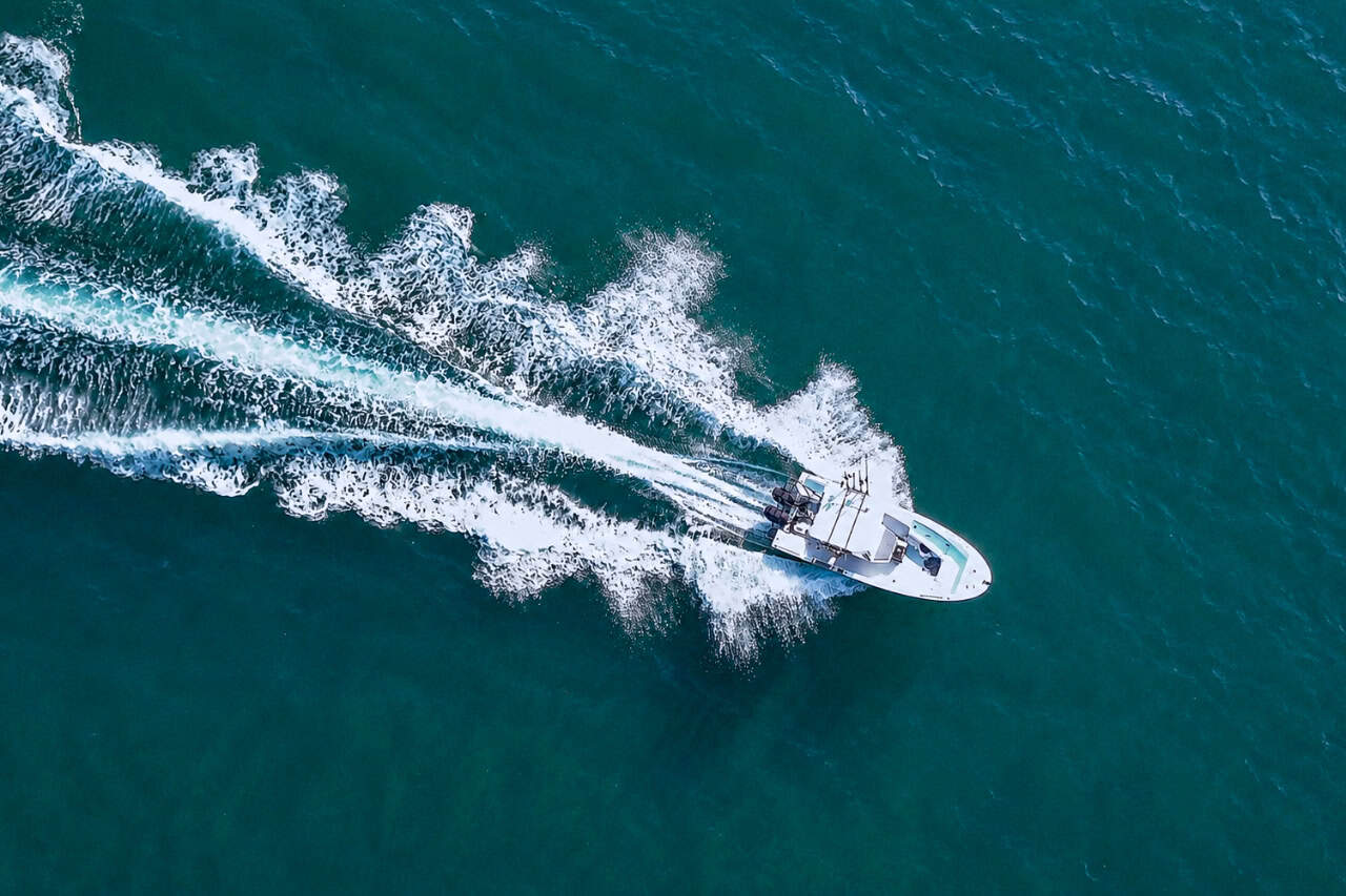 Alt Text: Aerial drone view of a private wakeboard boat cruising across the Atlantic Ocean in Tenerife, leaving a long white wake through clear turquoise waters.