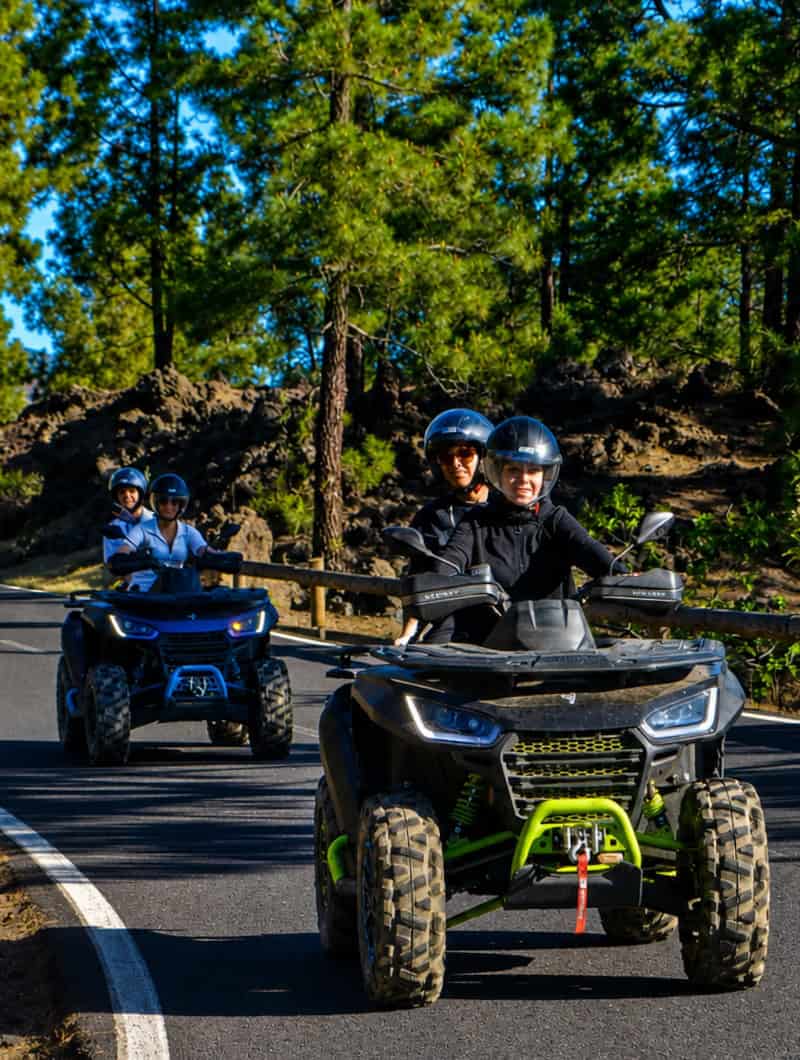 Quad safari Tenerife group riding powerful quads on a paved forest road through pine trees toward Mount Teide