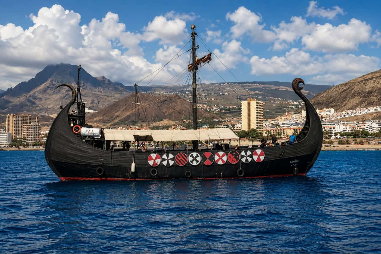 Traditional Viking-style longship sailing along the Tenerife coastline with Costa Adeje and surrounding mountains in the background during a sightseeing cruise.
