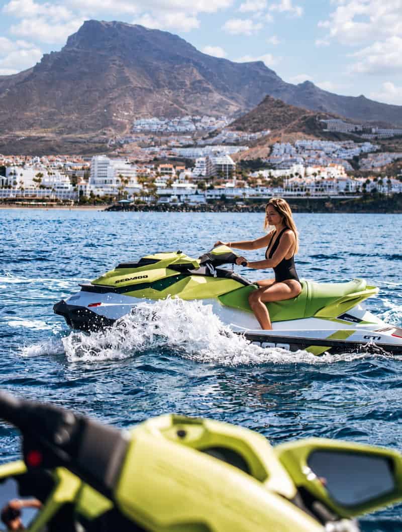 Woman riding a green Sea-Doo jet ski during a relaxed Tenerife jet ski safari with coastal views and mountains in the background.