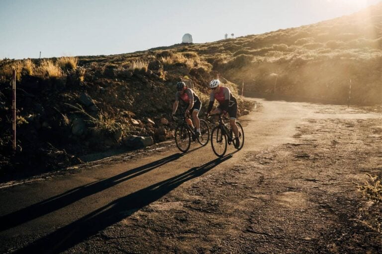 Two cyclists on a high altitude volcanic road in La Palma with an observatory on the ridge