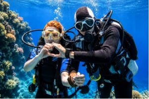 Two scuba divers underwater during a diving course in Tenerife, surrounded by coral reef and clear blue water while completing their diving licence training.