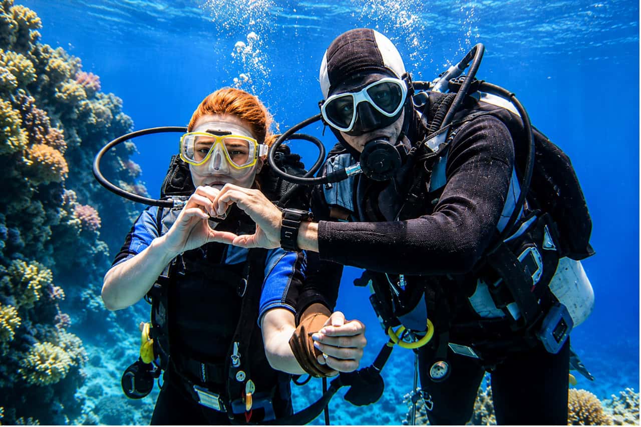Two scuba divers underwater during a diving course in Tenerife, surrounded by coral reef and clear blue water while completing their diving licence training.