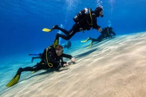 Group of scuba divers swimming over a sandy seabed in crystal-clear blue water during a guided dive in Fuerteventura