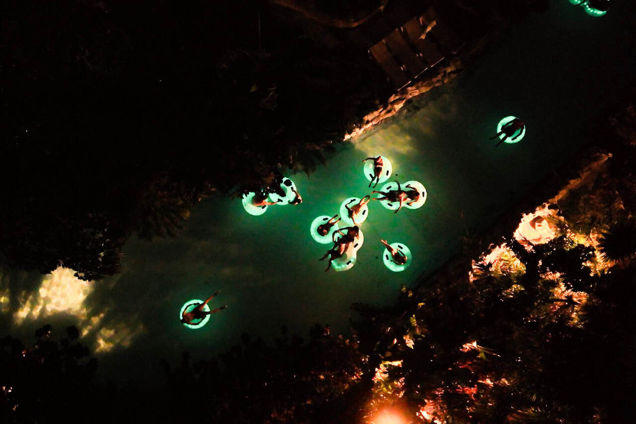 Aerial view of guests floating on glowing green rings in the dark pool at Siam Park Night in Tenerife