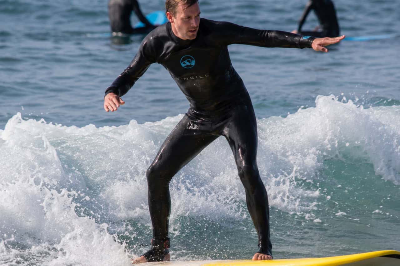 Beginner surfer riding a small wave during a surf lesson in Tenerife with an instructor nearby.