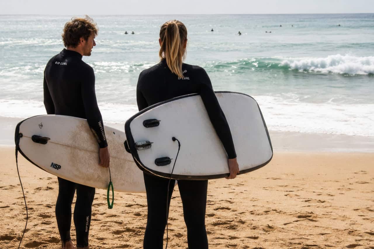 Two surf students carrying surfboards as they walk along the beach before a surfing lesson in Tenerife.