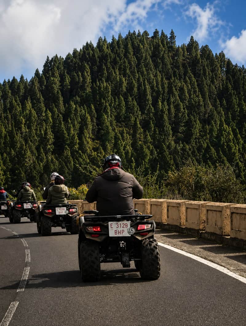 Guided Teide quad safari in Tenerife with riders driving on scenic mountain roads through pine forests toward Mount Teide National Park