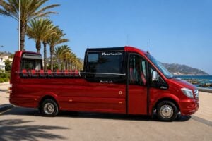 Red panoramic sightseeing bus parked along a palm-lined seafront promenade, ready for a guided coastal tour with open-air seating and scenic ocean views.