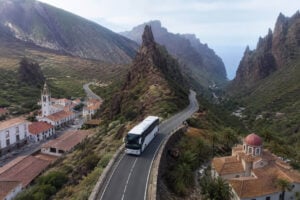 Aerial view of a sightseeing bus driving through Tenerife's dramatic mountain landscape, traditional villages, and scenic coastal roads.