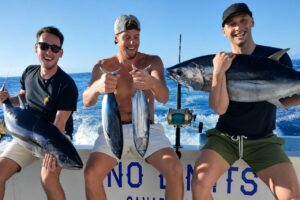 Three anglers smiling on a sport fishing boat while holding freshly caught tuna during a deep sea fishing trip.
