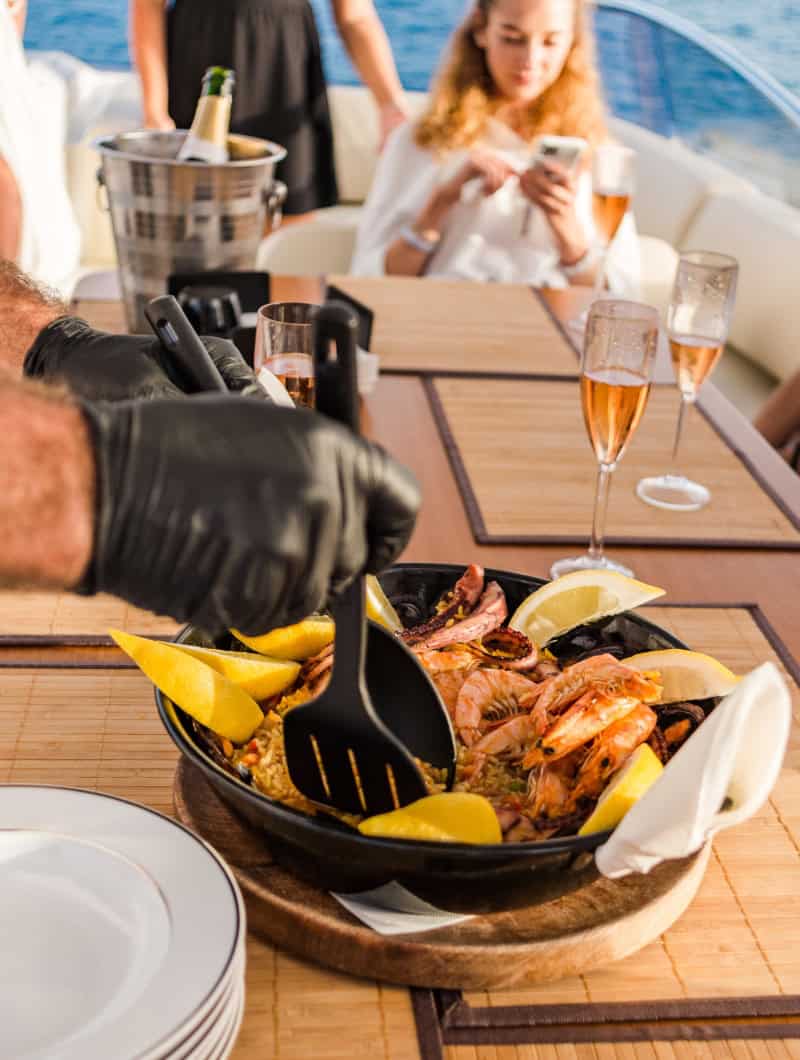 A crew member serving seafood paella to guests on the Tigresa yacht in Tenerife with Club Canary