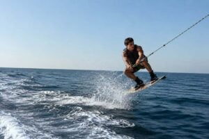 Wakeboarder performing a controlled jump behind a private wakeboard boat in Tenerife on calm open water under clear blue skies.