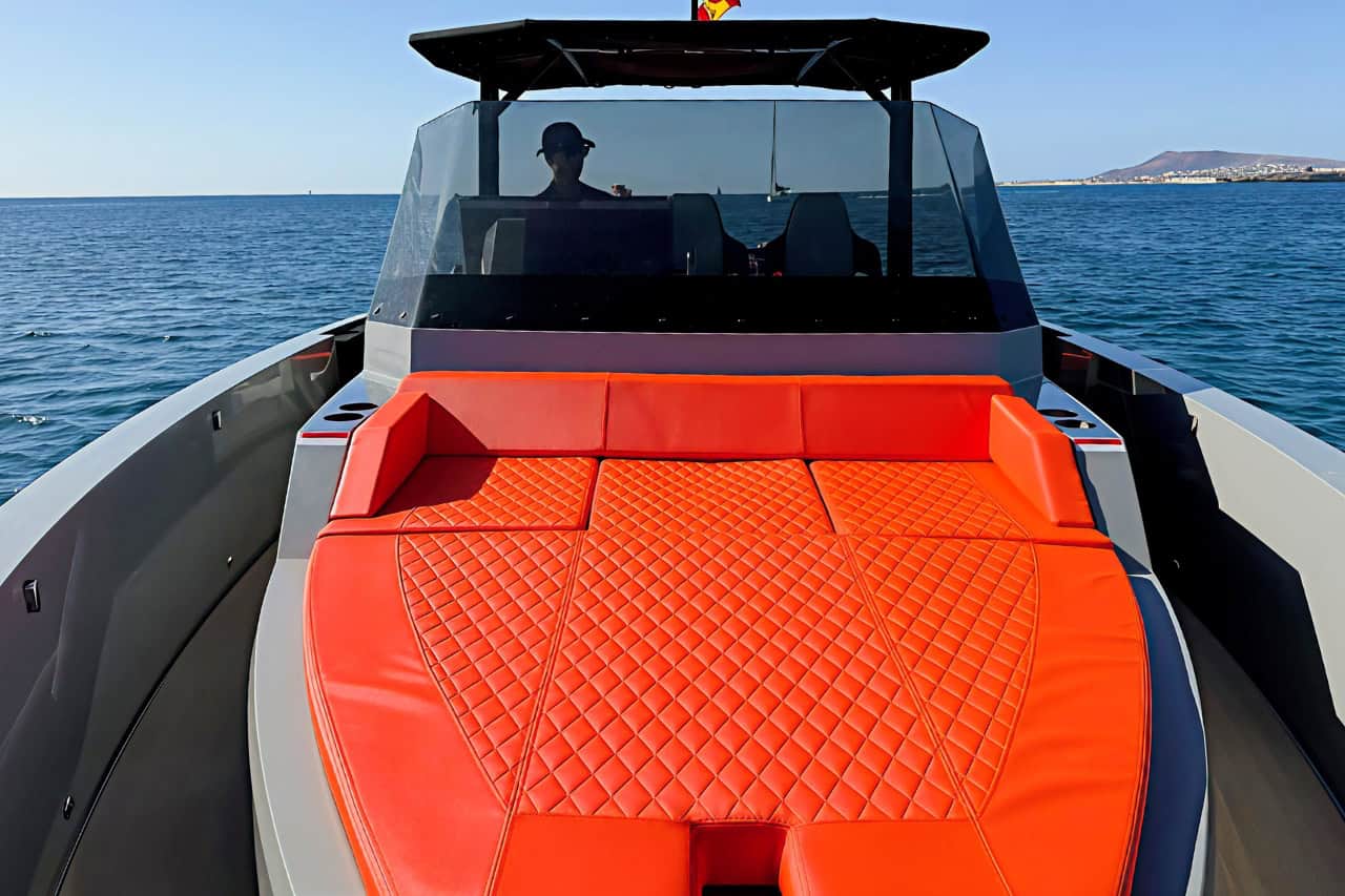 Front sunbed area of the BlackDune boat with orange cushions and the captain at the controls in Gran Canaria