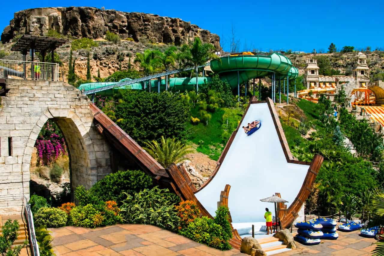 View of the large Boomerang water slide at Aqualand Maspalomas, with riders on an inflatable raft surrounded by tropical gardens and other water slides
