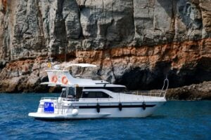 Моторная яхта Blue M совершает круиз вдоль вулканических скал Гран-Канарии, а пассажиры наслаждаются морской прогулкой вдоль побережья.