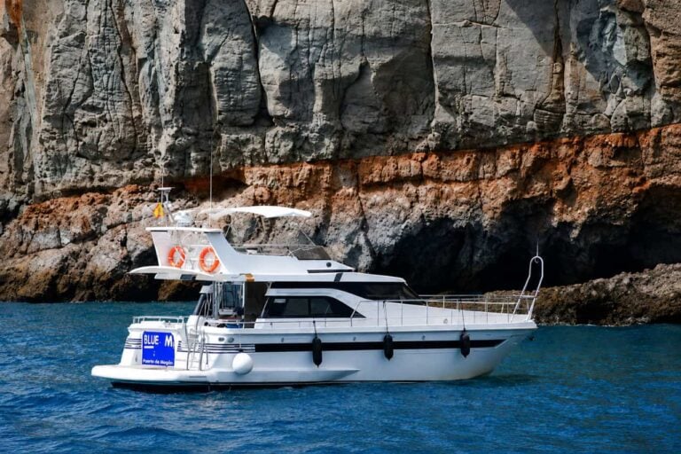 Blue M motor yacht cruising beside the volcanic cliffs of Gran Canaria with guests on deck