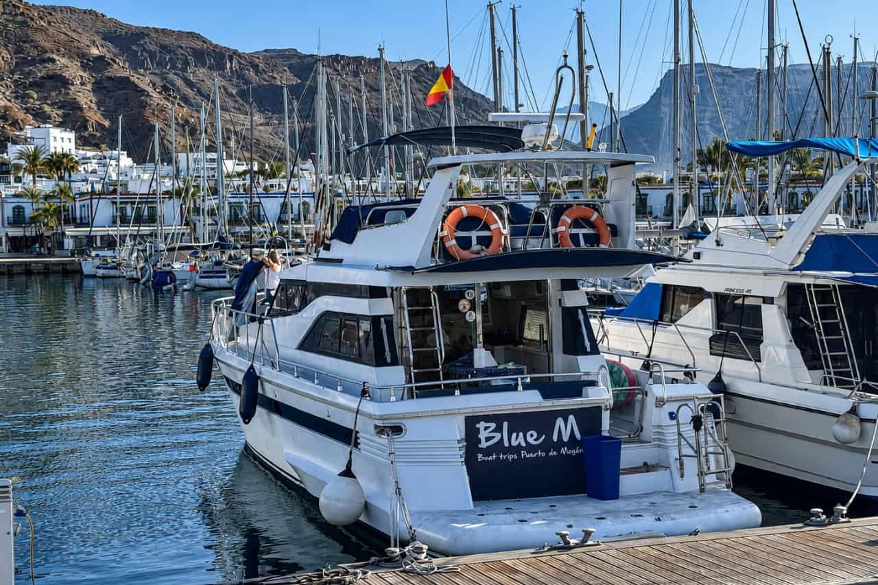 Blue M private yacht moored in Puerto de Mogán marina, Gran Canaria, surrounded by sailing boats and volcanic mountains.