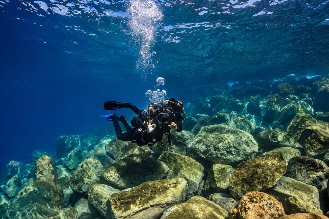 First-time scuba diver giving the OK hand signal above a rocky seabed