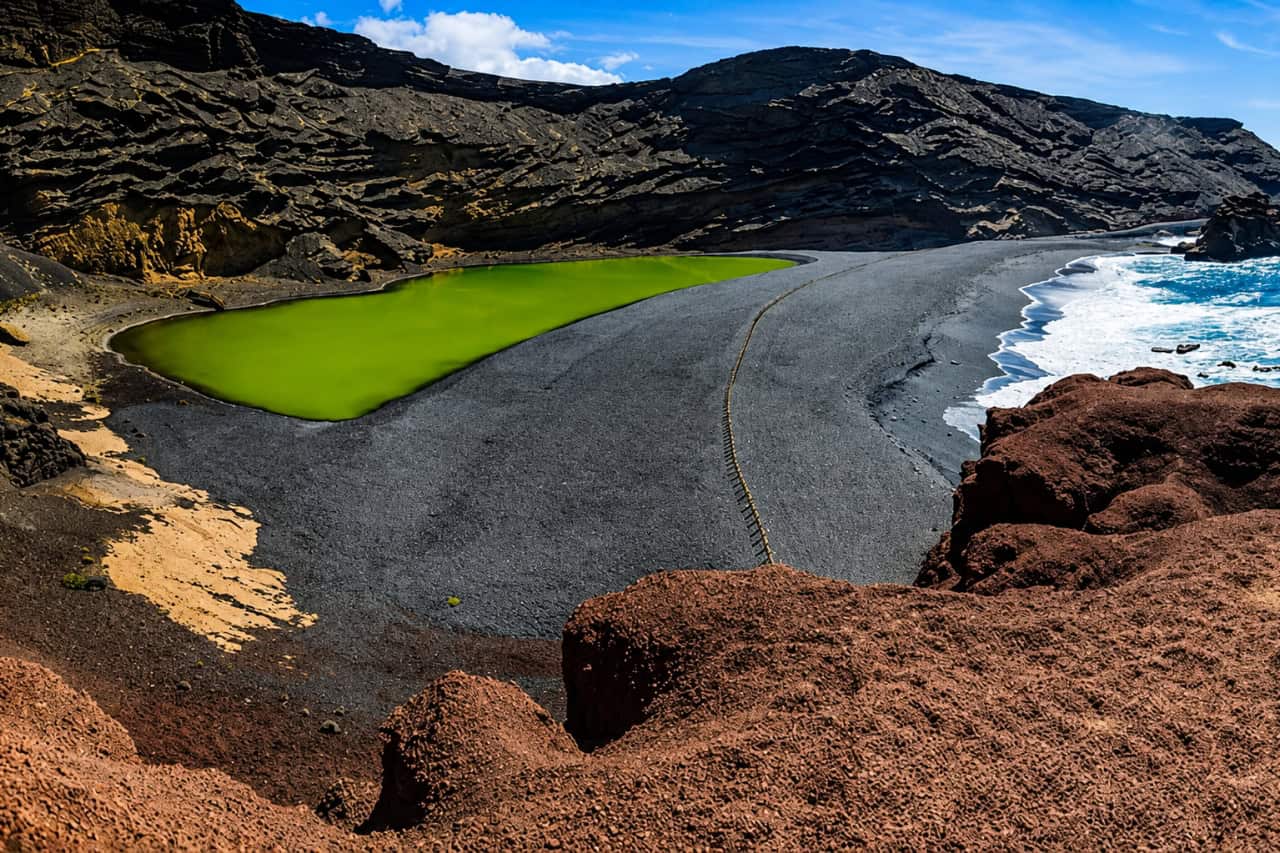 El Golfo green lagoon in Lanzarote surrounded by black volcanic sand, dramatic cliffs and the Atlantic Ocean.