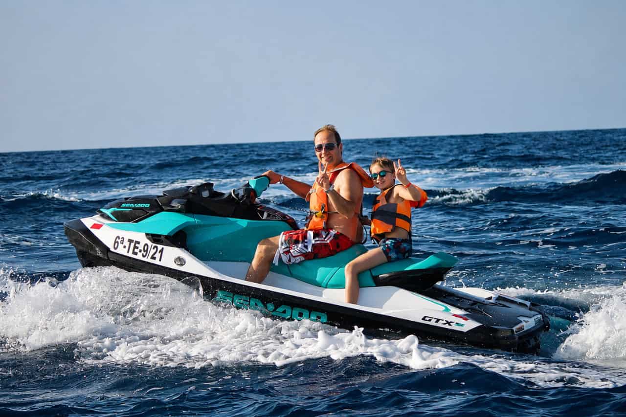 Adult and child enjoying a family jet ski safari in Tenerife on a turquoise Sea-Doo, riding together across the open ocean.