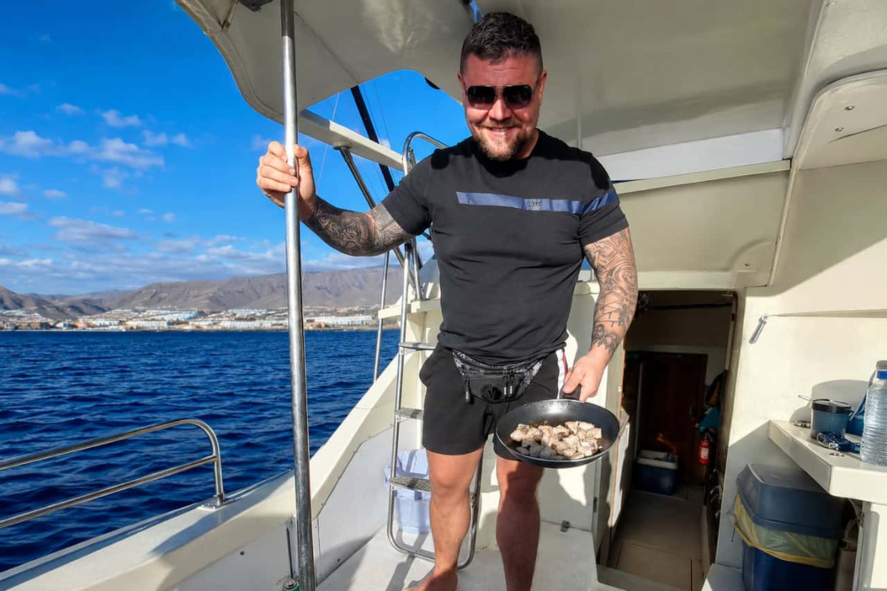 Crew member holding a pan of freshly prepared fish aboard a Tenerife sport-fishing boat.