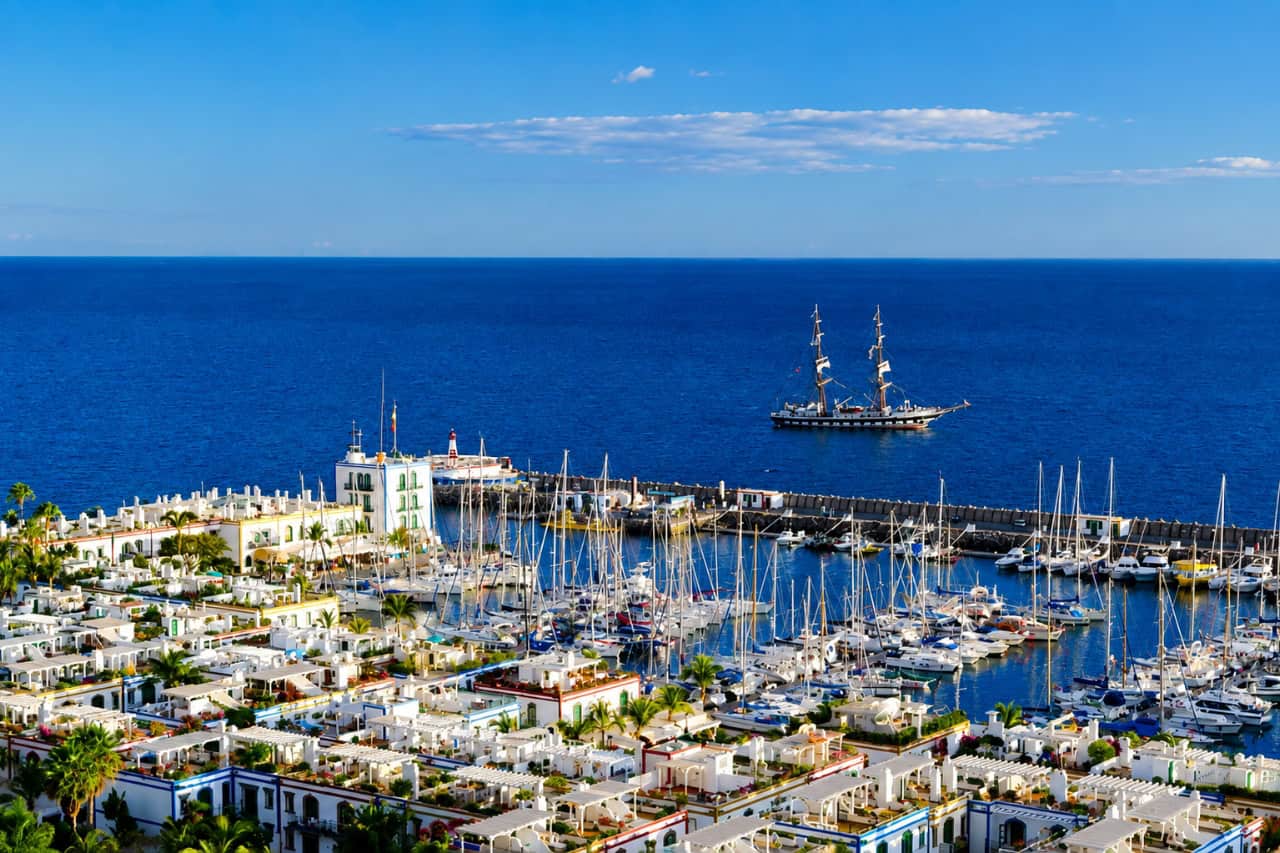 Puerto de Mogan marina with yachts and a sailing ship offshore
